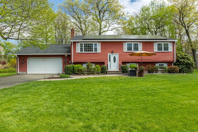 raised ranch with asphalt driveway, a chimney, an attached garage, a front lawn, and roof mounted solar panels