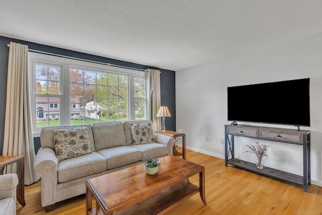 living room featuring light wood finished floors, baseboards, and a textured ceiling