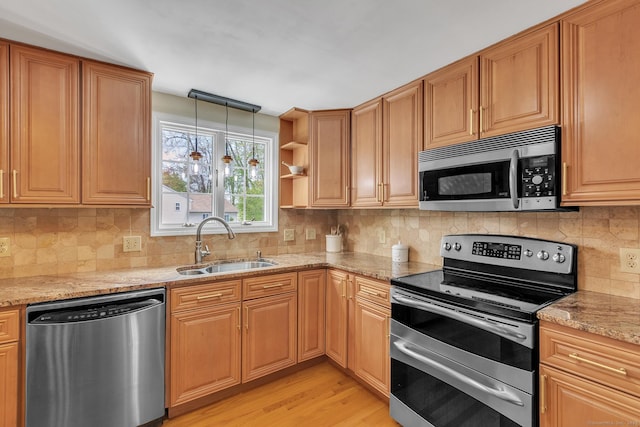 kitchen featuring stainless steel appliances, a sink, light wood-type flooring, light stone countertops, and tasteful backsplash