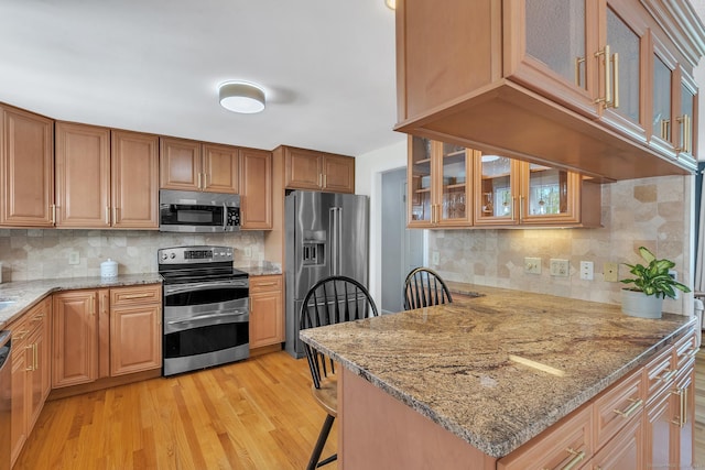 kitchen featuring appliances with stainless steel finishes, glass insert cabinets, a breakfast bar, and light stone countertops