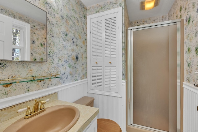 full bathroom with wallpapered walls, wainscoting, a shower stall, vanity, and a closet