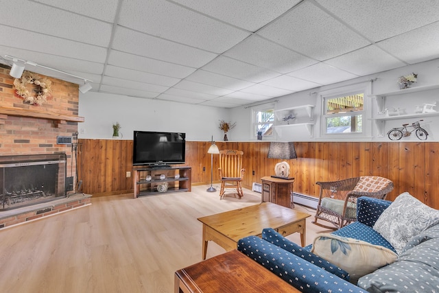 living room featuring wainscoting, wood finished floors, wooden walls, baseboard heating, and a paneled ceiling
