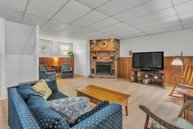 living area with wood finished floors, wooden walls, a drop ceiling, a fireplace, and a wainscoted wall