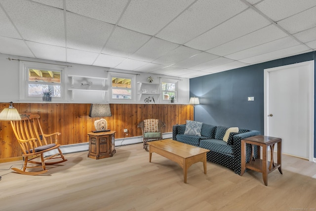 living area featuring light wood-style floors, a paneled ceiling, a baseboard radiator, wood walls, and wainscoting