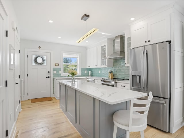 kitchen featuring wall chimney exhaust hood, appliances with stainless steel finishes, backsplash, light wood-style floors, and white cabinetry