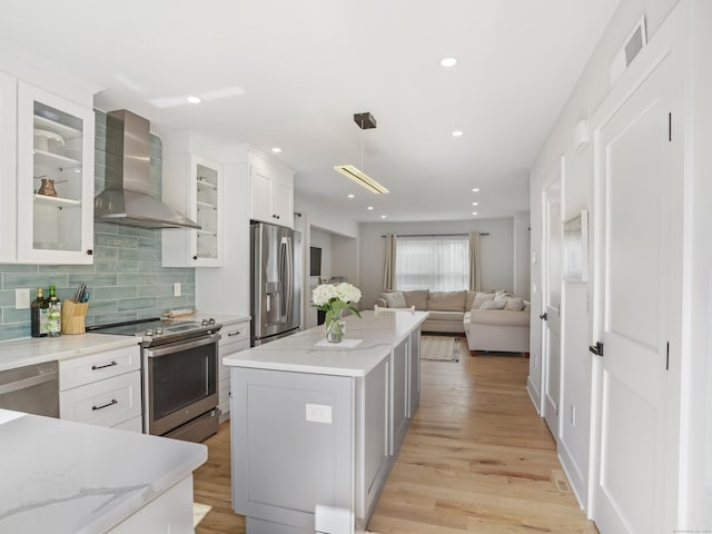 kitchen with stainless steel appliances, wall chimney exhaust hood, a kitchen island, backsplash, and white cabinetry