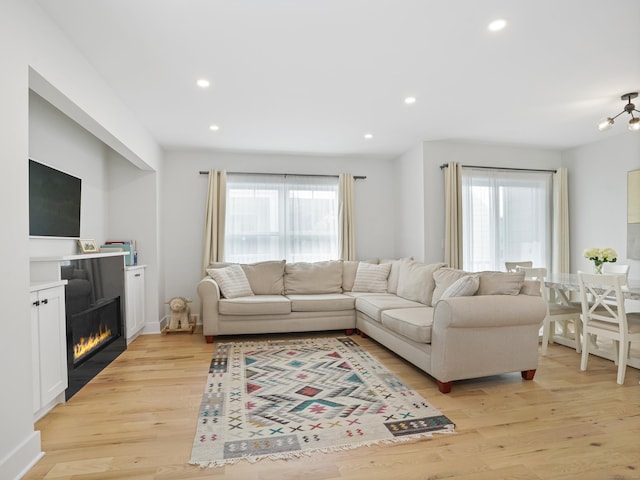 living room featuring healthy amount of natural light, light wood-style floors, recessed lighting, and a glass covered fireplace