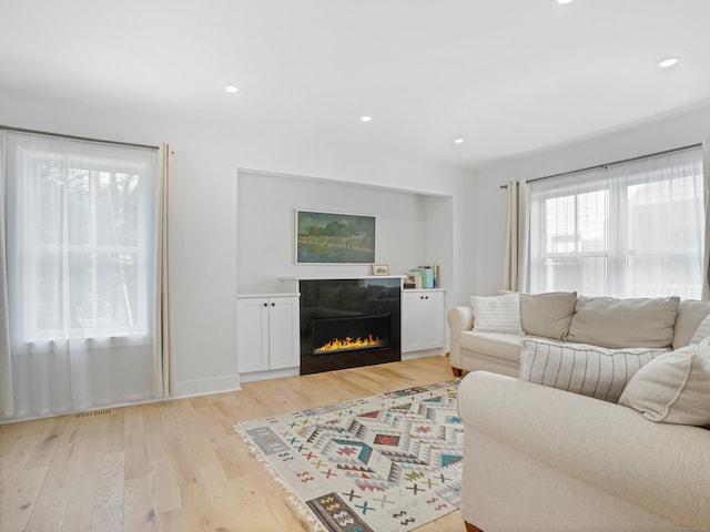 living room featuring light wood finished floors, a lit fireplace, and recessed lighting