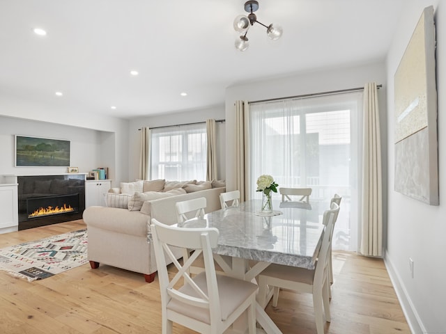 dining space with light wood-type flooring, a glass covered fireplace, recessed lighting, and baseboards