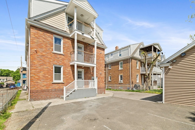back of property with a balcony, brick siding, and fence