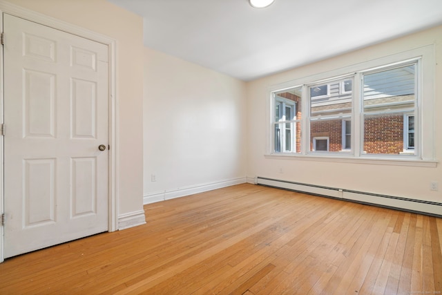 spare room featuring light wood-style floors, a baseboard heating unit, and baseboards