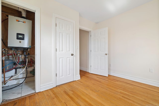 unfurnished bedroom with water heater, light wood-style flooring, and baseboards