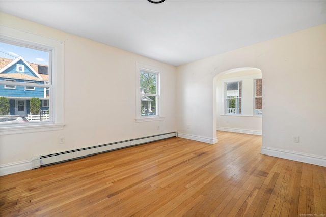 spare room with a baseboard heating unit, arched walkways, light wood-style flooring, and baseboards