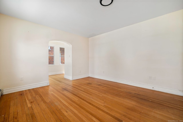 empty room featuring arched walkways, baseboards, and light wood-style floors