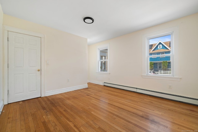 unfurnished room featuring baseboard heating, light wood-style floors, and baseboards