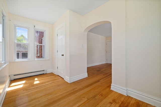 unfurnished room with a baseboard heating unit, arched walkways, light wood finished floors, and baseboards