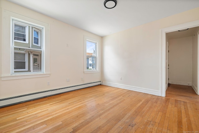 spare room featuring baseboard heating, light wood-type flooring, and baseboards