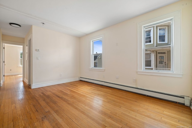 spare room featuring a baseboard heating unit, light wood-type flooring, and baseboards