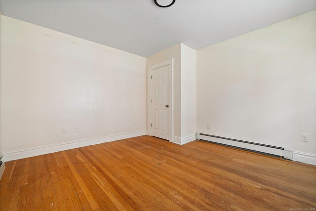 unfurnished room featuring a baseboard heating unit, light wood finished floors, and baseboards