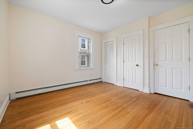 unfurnished bedroom featuring a baseboard heating unit, light wood-type flooring, two closets, and baseboards