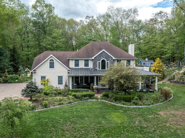 view of front of house featuring a standing seam roof, a chimney, covered porch, a front yard, and metal roof