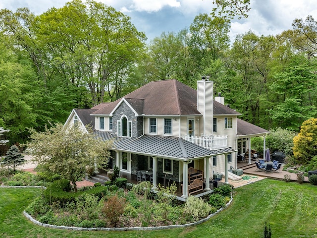 rear view of property featuring a standing seam roof, a chimney, metal roof, a lawn, and a wooden deck