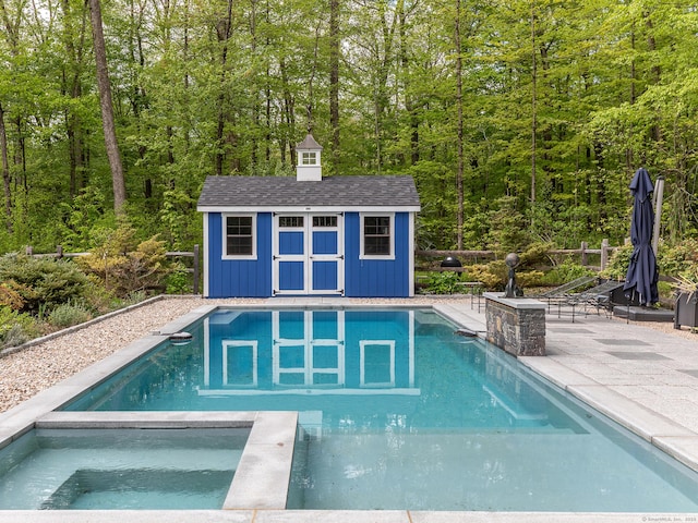 view of swimming pool featuring an outbuilding, a patio area, a view of trees, a storage unit, and a pool with connected hot tub