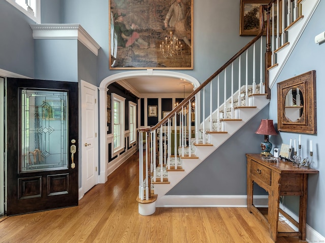 foyer entrance featuring arched walkways, a towering ceiling, wood finished floors, stairway, and baseboards