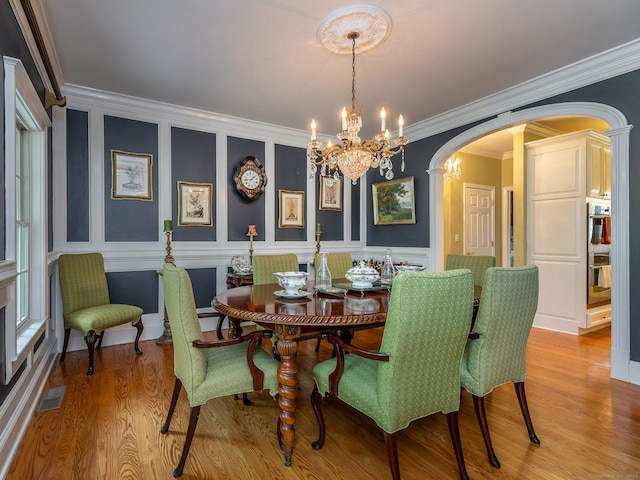 dining space with arched walkways, a chandelier, light wood-style flooring, crown molding, and a decorative wall