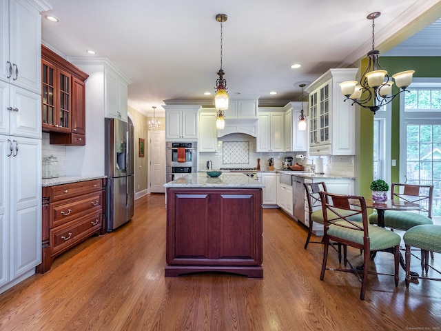 kitchen with stainless steel appliances, a chandelier, ornamental molding, wood finished floors, and backsplash