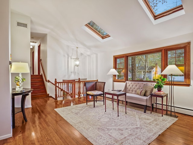 sitting room featuring a skylight, wood finished floors, a chandelier, baseboards, and stairs