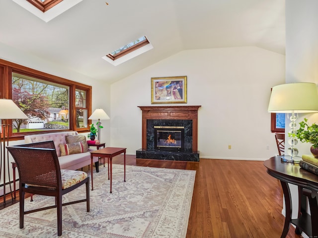 living room featuring a skylight, vaulted ceiling, a high end fireplace, wood finished floors, and baseboards