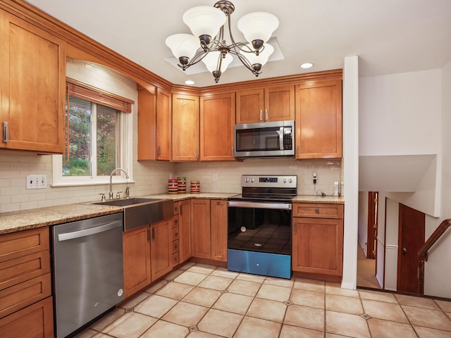 kitchen featuring appliances with stainless steel finishes, a sink, decorative backsplash, a chandelier, and brown cabinetry