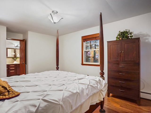 bedroom with wood finished floors, ensuite bath, and baseboard heating