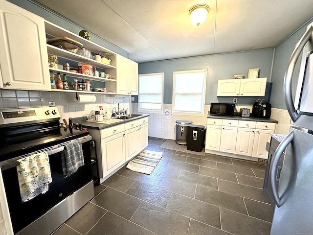 kitchen with appliances with stainless steel finishes, a sink, dark countertops, a wainscoted wall, and open shelves