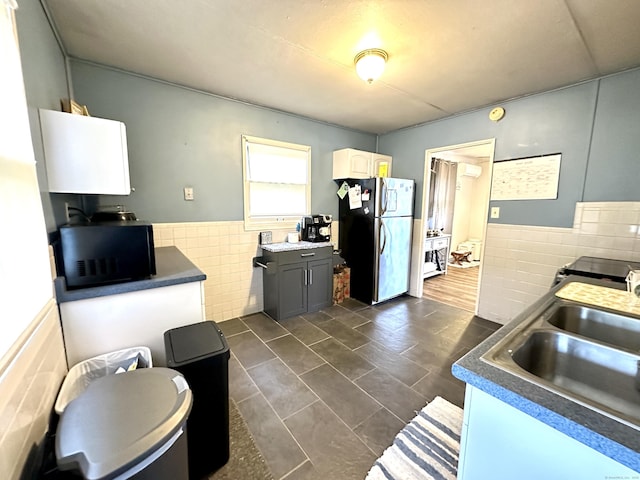 kitchen with freestanding refrigerator, black microwave, tile walls, a wainscoted wall, and a sink