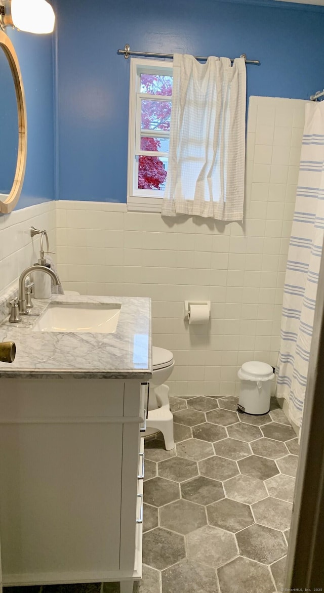 bathroom featuring tile walls, vanity, toilet, curtained shower, and wainscoting