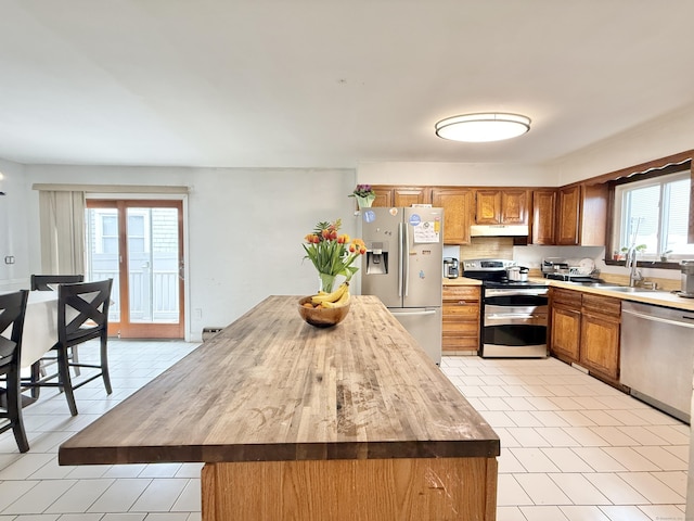 22 Palmer Ave, Stamford, CT 06902 - kitchen with stainless steel appliances, under cabinet range hood, a sink, light tile patterned floors, and brown cabinets
