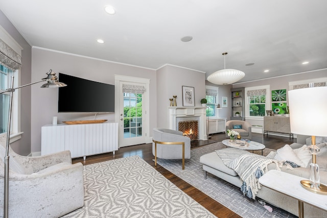 living area with wood finished floors, ornamental molding, recessed lighting, and a warm lit fireplace