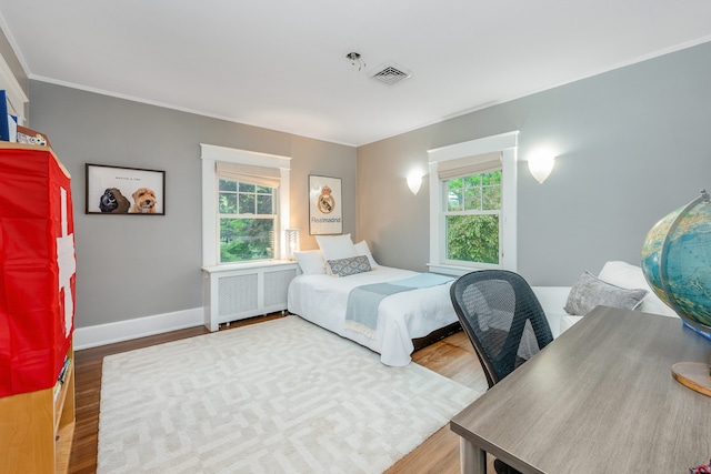 bedroom with radiator, wood finished floors, baseboards, and ornamental molding