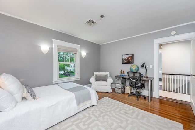 bedroom with wood finished floors, crown molding, and a desk