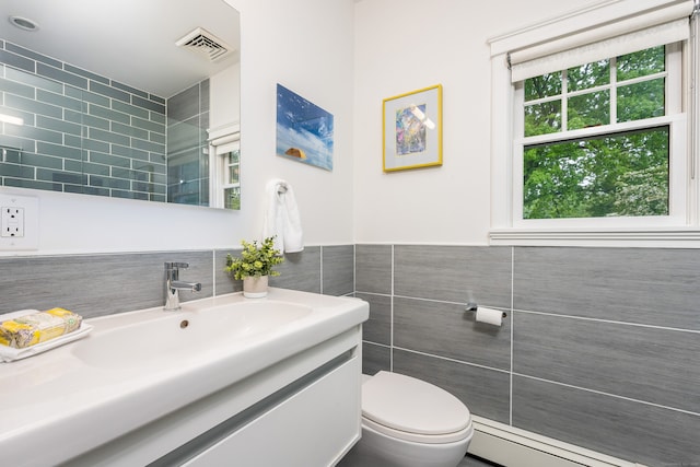 bathroom with tile walls, a baseboard heating unit, vanity, and toilet