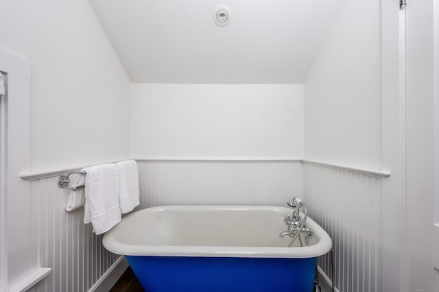 bathroom featuring a soaking tub, wainscoting, and wood finished floors