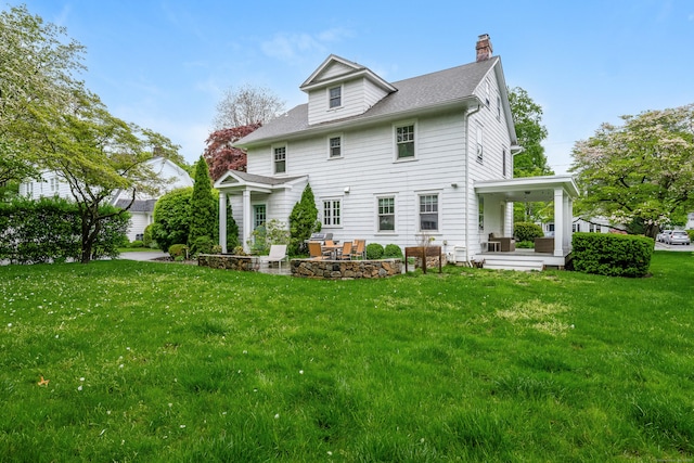 back of property featuring a yard, a chimney, a patio area, and roof with shingles