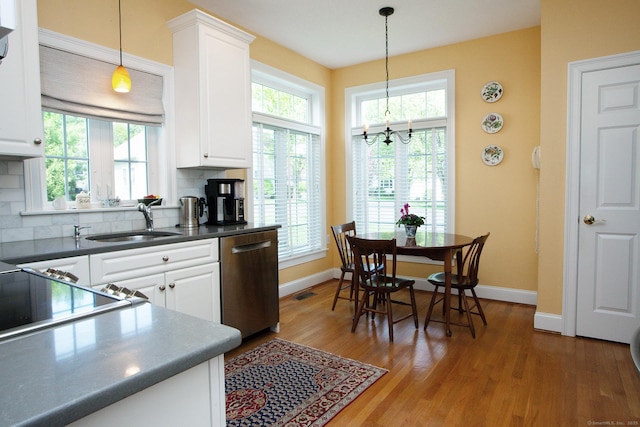 kitchen with stainless steel dishwasher, plenty of natural light, wood finished floors, and white cabinets