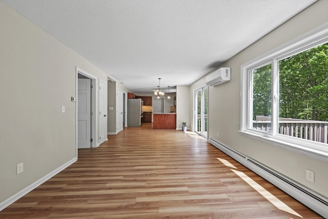 5 Nutmeg Ln, East Hampton, CT 06424 - unfurnished living room featuring baseboard heating, a wall unit AC, a chandelier, light wood-type flooring, and a textured ceiling