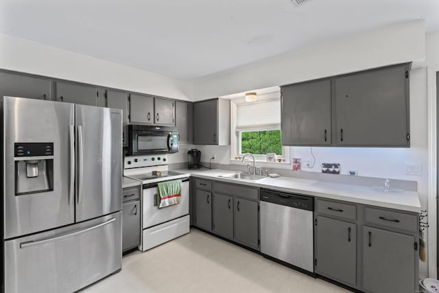 kitchen featuring appliances with stainless steel finishes, a sink, gray cabinetry, and light countertops