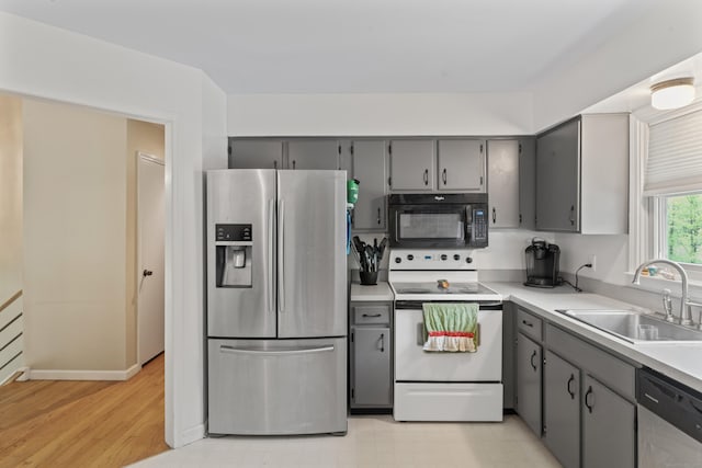 kitchen featuring stainless steel appliances, gray cabinetry, a sink, light countertops, and light wood-style floors