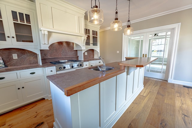 kitchen with a sink, light wood-style floors, backsplash, crown molding, and decorative light fixtures