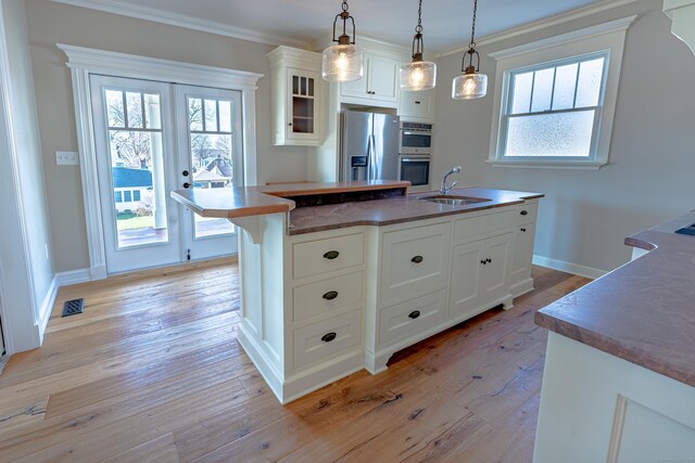 kitchen with a sink, stainless steel appliances, light wood finished floors, a center island with sink, and crown molding
